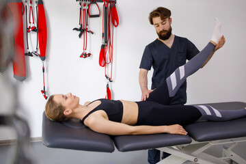 Chiropractor stretches a female patient leg. Male physiotherapist is helping woman stretching his...