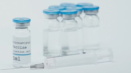 close up of syringe near bottles with coronavirus vaccine and lettering isolated on white.