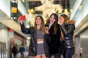 Christmas in the city at night, decoration in winter. Three friends enjoying smiling taking a selfie