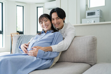 自宅で笑顔でお腹をさする日本人夫婦