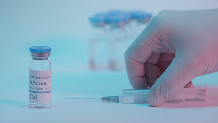cropped view of person taking syringe near bottles with coronavirus vaccine on blue.