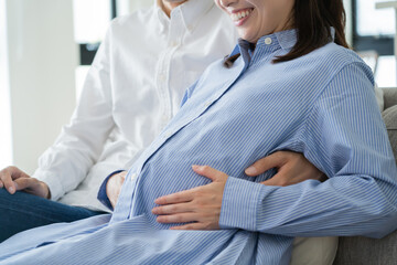 自宅で笑顔でお腹をさする日本人夫婦
