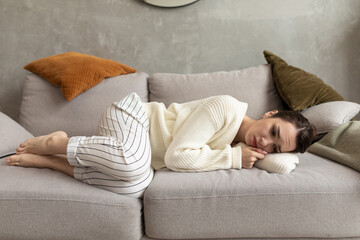 a young depressed woman lies on the couch curled up and cries