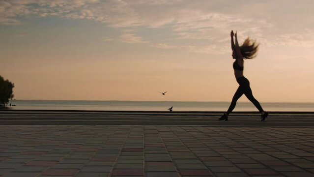 Young woman doing backflips.Girl doing acrobatic activity against the sea at sunrise. Fitness Lifestyle slow motion
