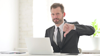 Young Businessman Showing Thumbs Down Sign While using Laptop in Office