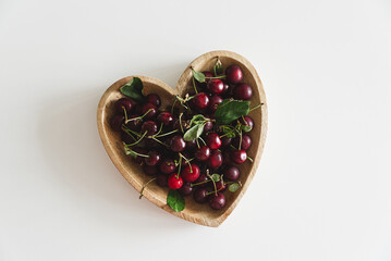 Heart shape bowl of fresh cherries on white wooden table. Top view