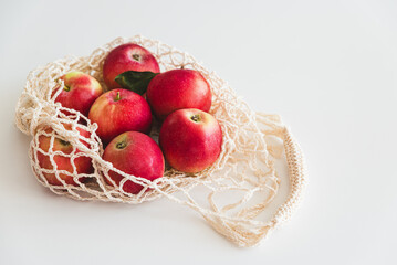 String bag with red ripe apples on white background. Top view