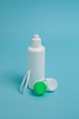 Packages with contact lenses, case, tweezers and drops on blue background