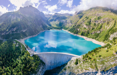 Water dam and reservoir lake in Swiss Alps mountains producing sustainable hydropower, hydroelectricity generation, renewable energy to limit global warming, aerial view, decarbonize, summer - obrazy, fototapety, plakaty