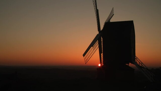 Sun setting on the horizon behind a traditional wooden windmill at sunset