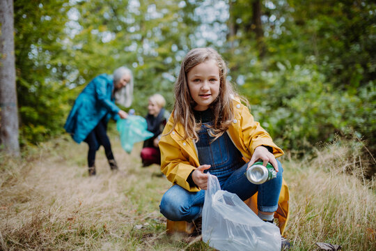 Small girl with mother and grandmother picking up waste outoors in forest.