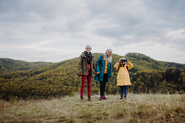Fototapeta na wymiar Happy small girl with mother and grandmother hiking outoors in autumn nature.