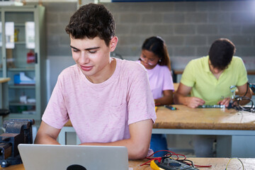 Cheerful portrait of a young white man at high school college using laptop to study in classroom