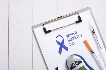Text World Diabetes Day and blue ribbon on tablet with glucometer and syringes on a wooden background, top view