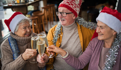 Happy senior friends indoors in cafe clinking champagne glasses and celebrating Christmas.