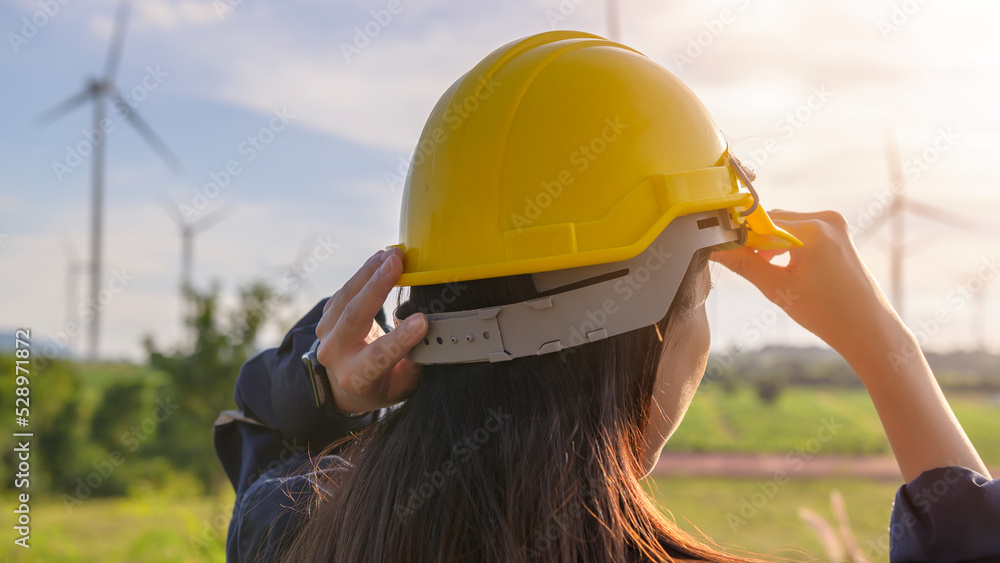 Wall mural a woman engineer is putting a protective helmet on her head at sunset.