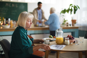 Elderly woman enjoying breakfast and reading newspaper in nursing home care center.