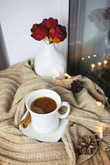 Black coffee in a white mug with cinnamon sticks. A romantic setting on the table beautifully stands coffee and a vase of red roses.