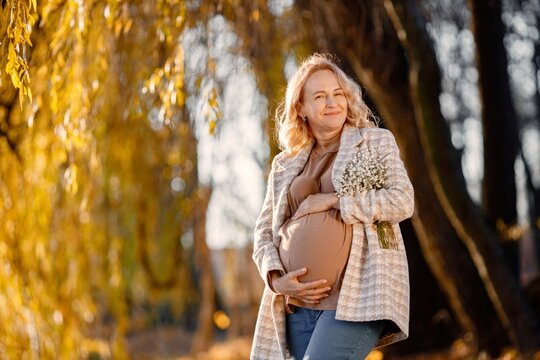 Caucasian mature pregnant woman standing in autumn park