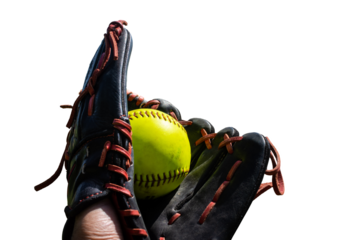 a green softball sits in a red and black leather glove outside on a sunny day 
