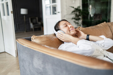 A woman audiobook is resting at home listening to a playlist of music with headphones in the app