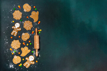 Halloween holiday gingerbread cookies on dark background. Baking ingredients and utensils - flour, rolling pin, gingerbread, milk, eggs. Making Halloween party sweet cookies. Top view copy space