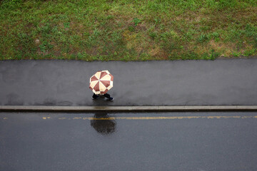 Rain in a city, lonely woman with umbrella walking down wet sidewalk, top view. Rainy weather at...