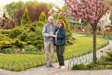 Obraz premium Mature elderly couple in summer park, senior couple standing in spring summer or autumn time. Healthcare lifestyle elderly retirement love couple together valentines day concept