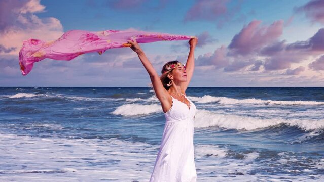 Cinemagraph of woman in white dress walking on the beach with  a shawl in the wind

