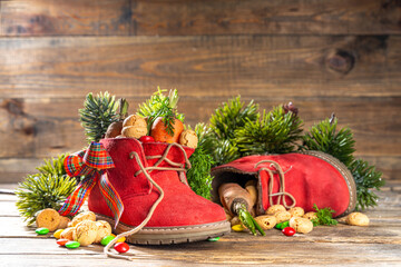 Sinterklaas, Saint Nicholas day background. Little kid red shoe with carrots and sweets, trooigoed, pepernoten, candy. Dutch Christmas holiday on cozy wooden background.