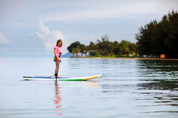 Fototapeta na wymiar Child on stand up paddle. Water and beach sport