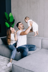 Obraz premium Proud mother and father smiling at newborn baby daughter, sitting on the sofa at home