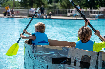 Two boys paddling a cardboard boat in a race in a pool