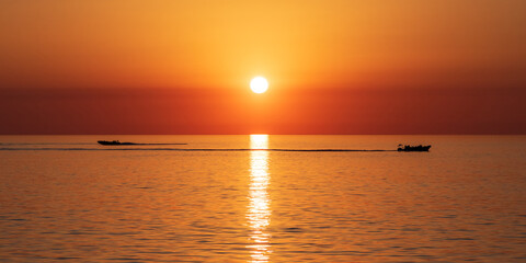 boats travelling in opposite directions through reflection of sunlight during sunset over sea.