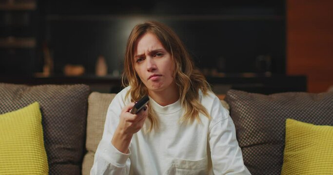 Tired woman changing boring television channels, yawning, sitting on sofa, resting at home after hard working day