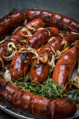 Grilled sausages with onion and herbs served on a plate, close-up. Roasted, fried meat sausages.