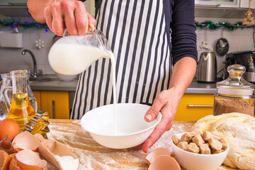 Woman pastry chef in a striped culinary apron pours milk while making homemade baking, close up