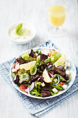 Salad with Grilled Beef Pieces, Cherry Tomatoes, feta Cheese and Kalamata Olives. Bright wooden background. Close up.	