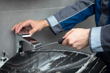 Close up photo of plumber hands with screwdriver fixing faucet in the bathroom. Handyman repairs a water tap