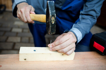 Close up of hands of carpenter holding hammer and knocking in nail the wood	