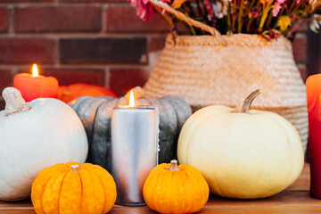 Festive composition for autumn holidays. Burning candle, various pumpkins and flowers bouquet in the wicker basket on brik wall background. Thanksgiving or Halloween. Fall Harvesting. Selective focus