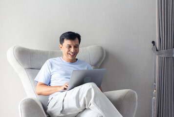 Happy Asian man using Pc Laptop computer on sofa in home