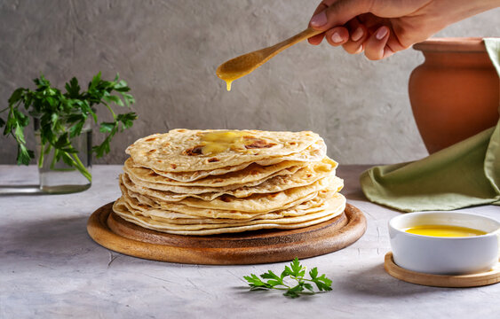 Homemade Indian Chapati or Roti on grey concrete background with human hand pouring butter ghee over 