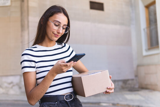 Smiling female courier photographing parcel on street