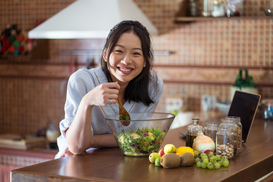 Content young ethnic woman eating salad from bowl in kitchen