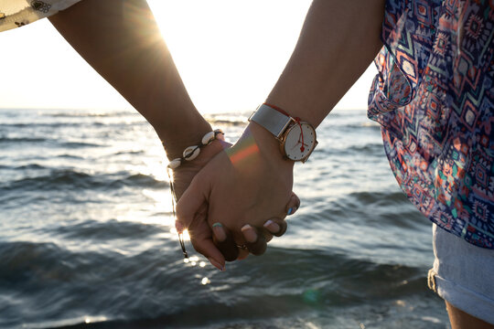Crop lesbian couple holding hands near sea