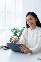 Portrait of Young Asian woman hand freelancer is working her job on computer tablet in modern office. Doing accounting analysis report real estate investment data, Financial and tax systems concept.