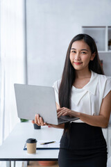 Beautiful Asian businesswoman holding a laptop computer and looking at the camera.
