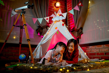 Asian mother stay with her daughter and read book in area look like amusement area for child compose of pavilion or tent with concept happy activity together at home. © narong