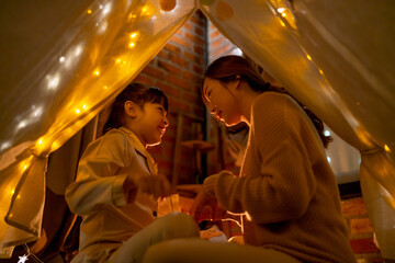 Asian mother and daughter enjoy together in tent and fun during holiday night.